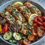 Perfectly cooked Sheet Pan Salmon and Veggies Bowl with vibrant red onions, carrots, bell peppers, and cherry tomatoes on a rustic wooden table.