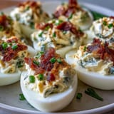 Cream cheese-stuffed jalapeño popper deviled eggs garnished with fresh jalapeño slices and chives.  