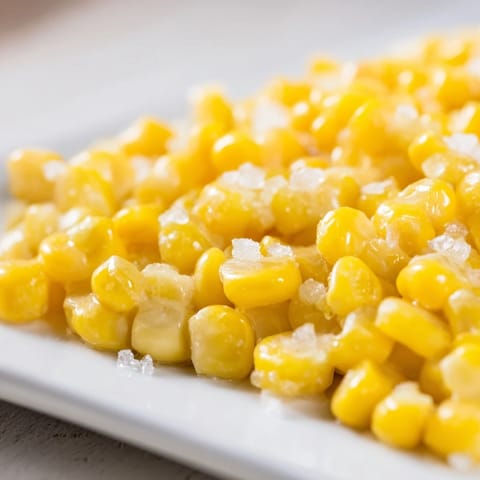 Freshly boiled sweet corn on the cob with melted butter and a sprinkle of salt, served hot on a sunny picnic table.