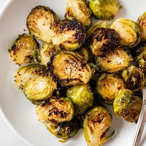 Roasted Brussels Sprouts are spread on a baking sheet next to olive oil and seasonings before roasting.