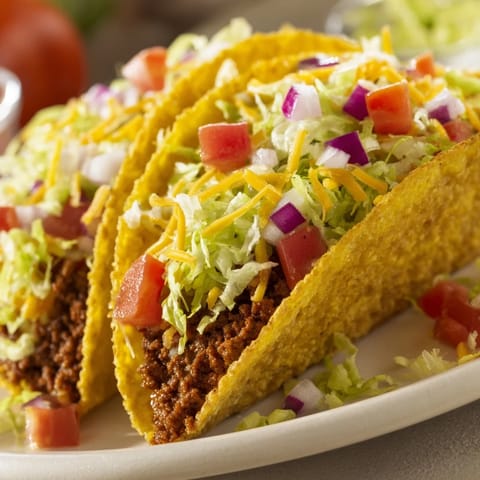 Loaded American-Style Tacos topped with crisp lettuce, diced tomatoes, and melty cheddar on a rustic table.