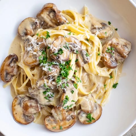 A close-up of Creamy Mushroom Alfredo, featuring fettuccine coated in luscious sauce with garlic, mushrooms, and fresh parsley.