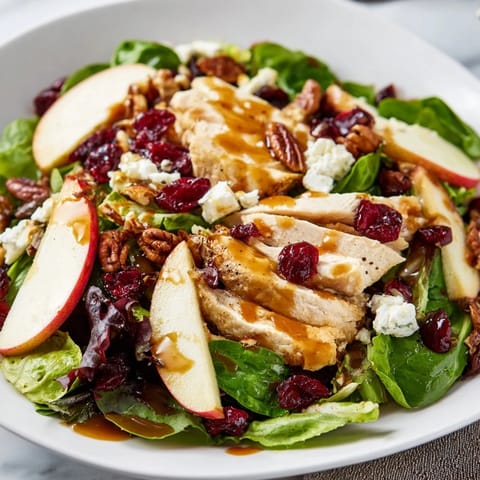 Golden dressing glistens over a vibrant Caramel Apple Chicken Salad, featuring red onion, dried cranberries, and crumbled feta for a festive autumn meal.