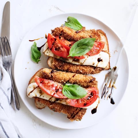 A close-up of the Crispy Chicken Caprese Sandwich, drizzled with balsamic glaze and olive oil, served beside a glass of red wine.