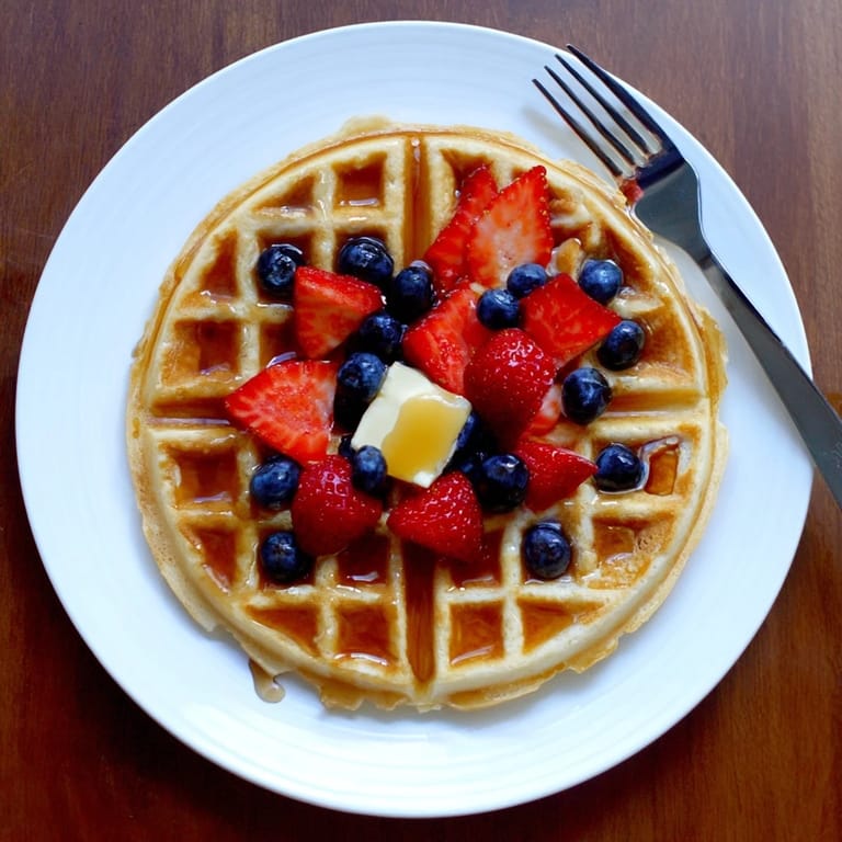 Golden brown homemade waffles stacked high, steam rising from the fluffy insides, ready for a generous pour of butter and warm maple syrup.