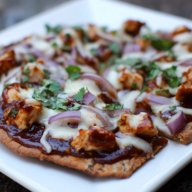 A close-up of BBQ Chicken Flatbread with gooey cheese and tangy sauce, sliced into wedges on a rustic wooden board.  