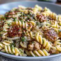 A close-up of Winter Pasta with Sausage and Fennel in a white bowl, featuring golden penne pasta coated in a glossy white wine sauce with savory sausage crumbles and tender, caramelized fennel slices.