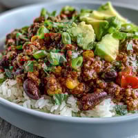Steaming bowl of hearty Chili Bowl Base served over fluffy white rice with shredded cheese.