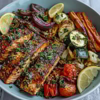 Golden-brown roasted salmon fillets and caramelized vegetables from the Sheet Pan Salmon and Veggies Bowl, garnished with fresh parsley and lemon wedges.