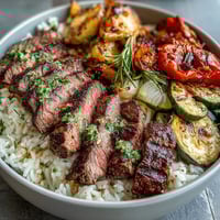 Freshly grilled steak slices rest atop fluffy white rice with colorful roasted vegetables on a wooden table, with chimichurri sauce being drizzled over the Grilled Steak Bowl.